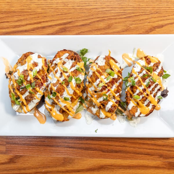 Four loaded potato skins with white and orange sauce, and green onions on a white rectangular plate.