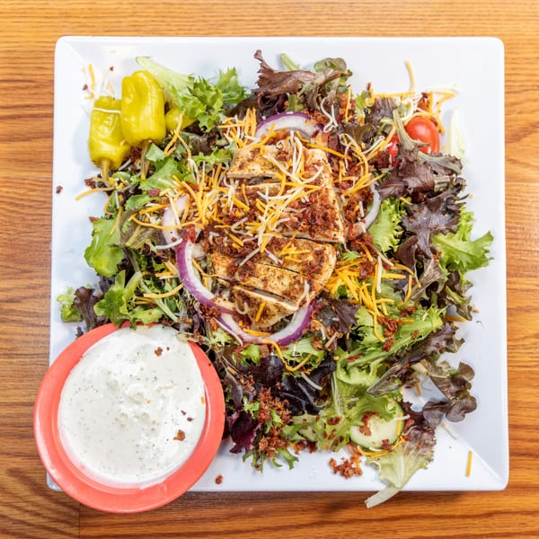 Grilled chicken salad with mixed greens, cheese, bacon, red onion, tomatoes, and a side of ranch.
