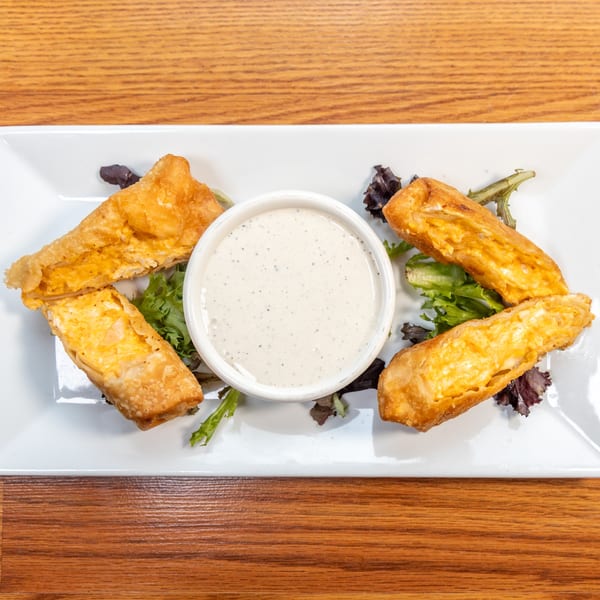 Four golden-fried egg rolls with creamy filling, served with a side of ranch dressing and lettuce.