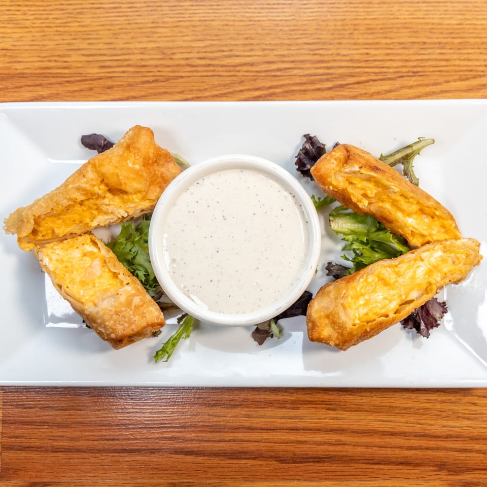 Four golden-fried egg rolls with creamy filling, served with a side of ranch dressing and lettuce.