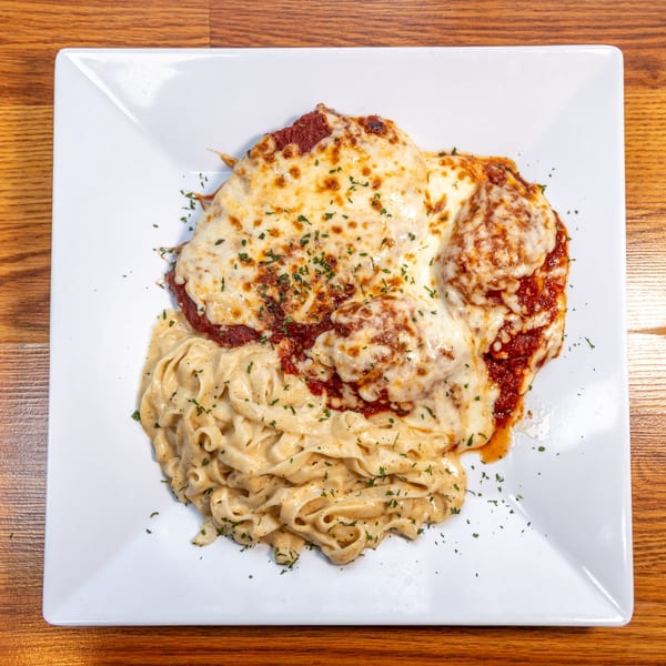 Chicken parmesan with melted cheese and marinara sauce, served alongside creamy fettuccine pasta.