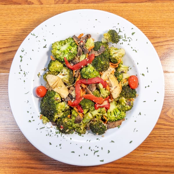 A white plate filled with a colorful vegetable medley of broccoli, red peppers, mushrooms, and cherry tomatoes.