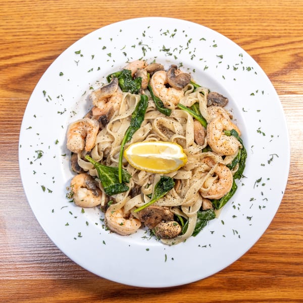 Fettuccine pasta with shrimp, spinach, mushrooms, and a lemon wedge on a white plate.