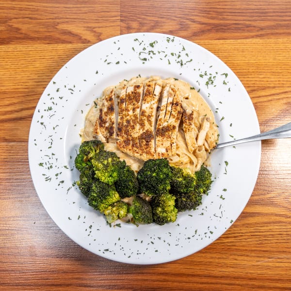 Cajun chicken pasta with broccoli florets on a white plate, garnished with parsley, on a wooden table.